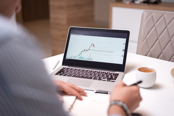 a person sitting holding a pen in his hand and analyzing a marketing trend graph on a laptop