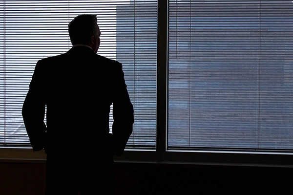a person standing with his hands in pockets facing and looking at the building from the glass window